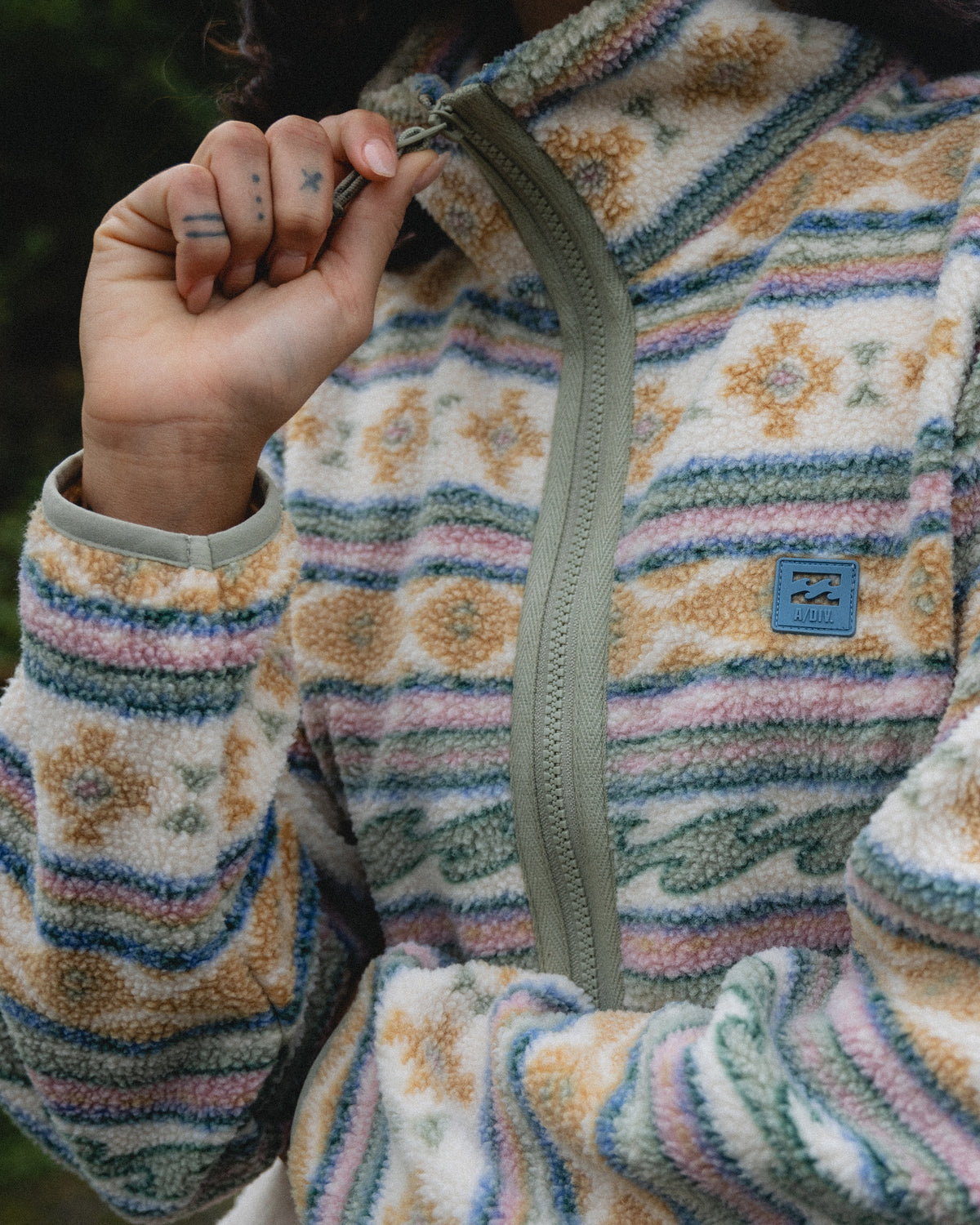 Cream sherpa fleece with multicolor geometric stripes, full-zip front, mock neck, and blue brand label visible.