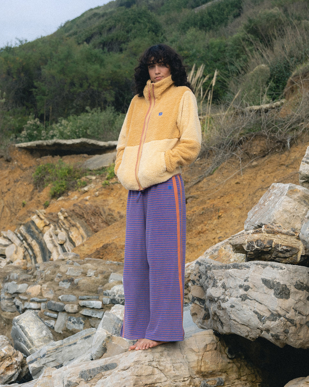 Iris terry pants with horizontal stripes worn with a yellow fleece jacket in an outdoor rocky setting.