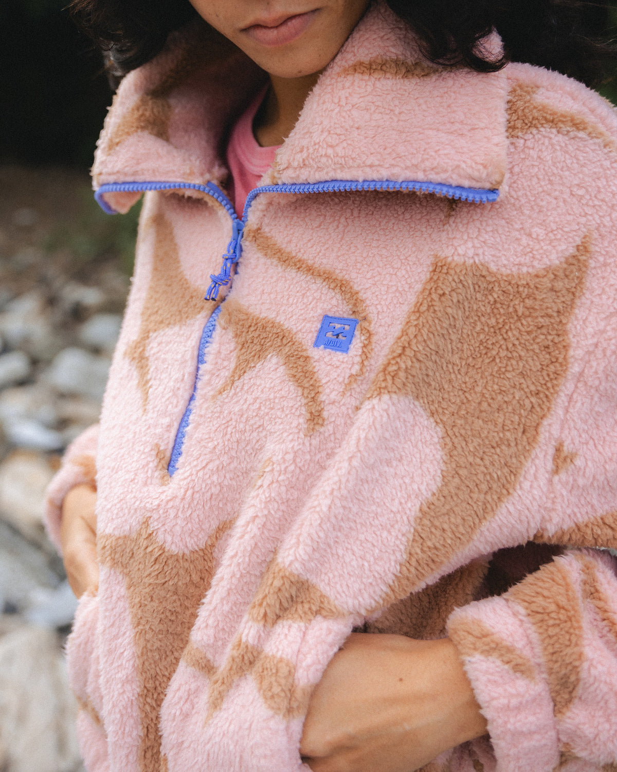 Rose brown sherpa fleece with tan geometric pattern, half-zip closure with blue cord, and small blue brand label.
