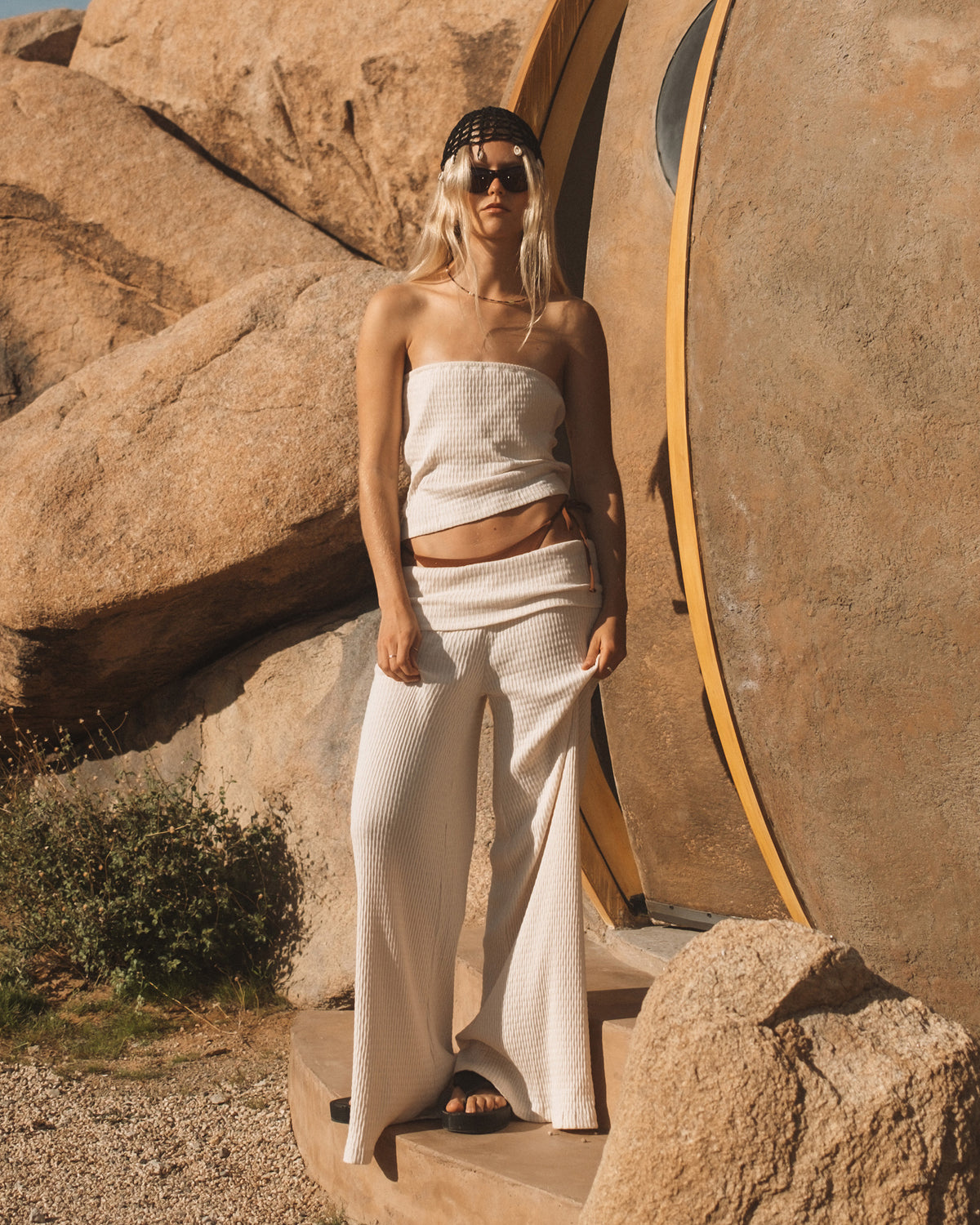 White ribbed tube top with matching high-waisted pants, worn with black cap and sunglasses.