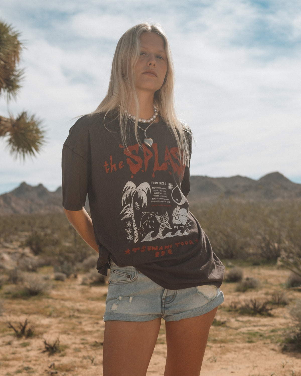 Person wearing off-black short sleeve t-shirt with graphic design and denim shorts in desert landscape.