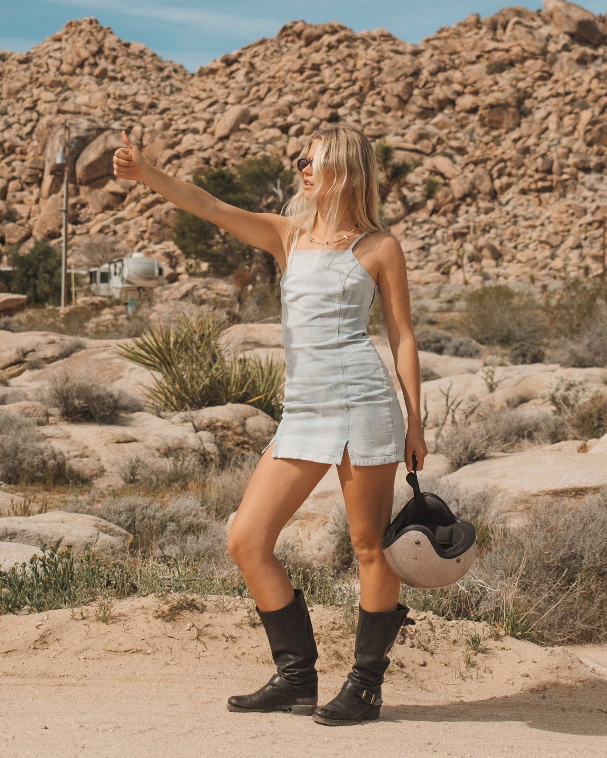 Light blue denim sleeveless dress with front button closure and side slit, worn with black boots.