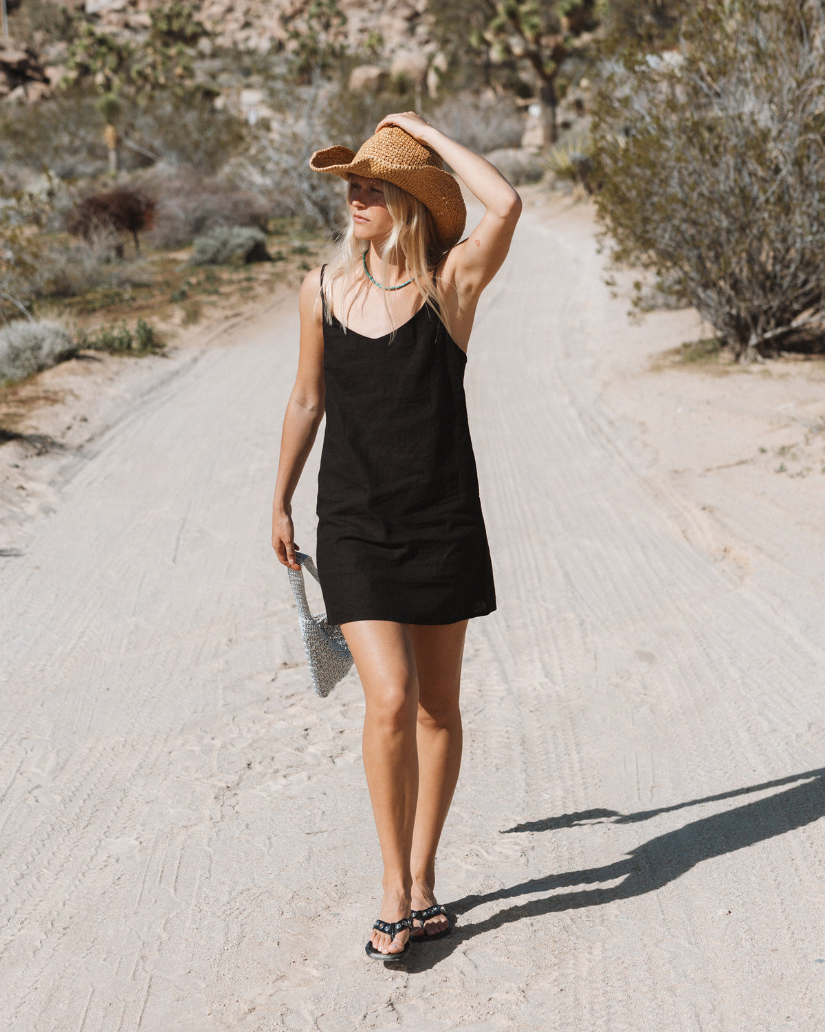 Black sleeveless slip dress with V-neckline worn on a dirt road.