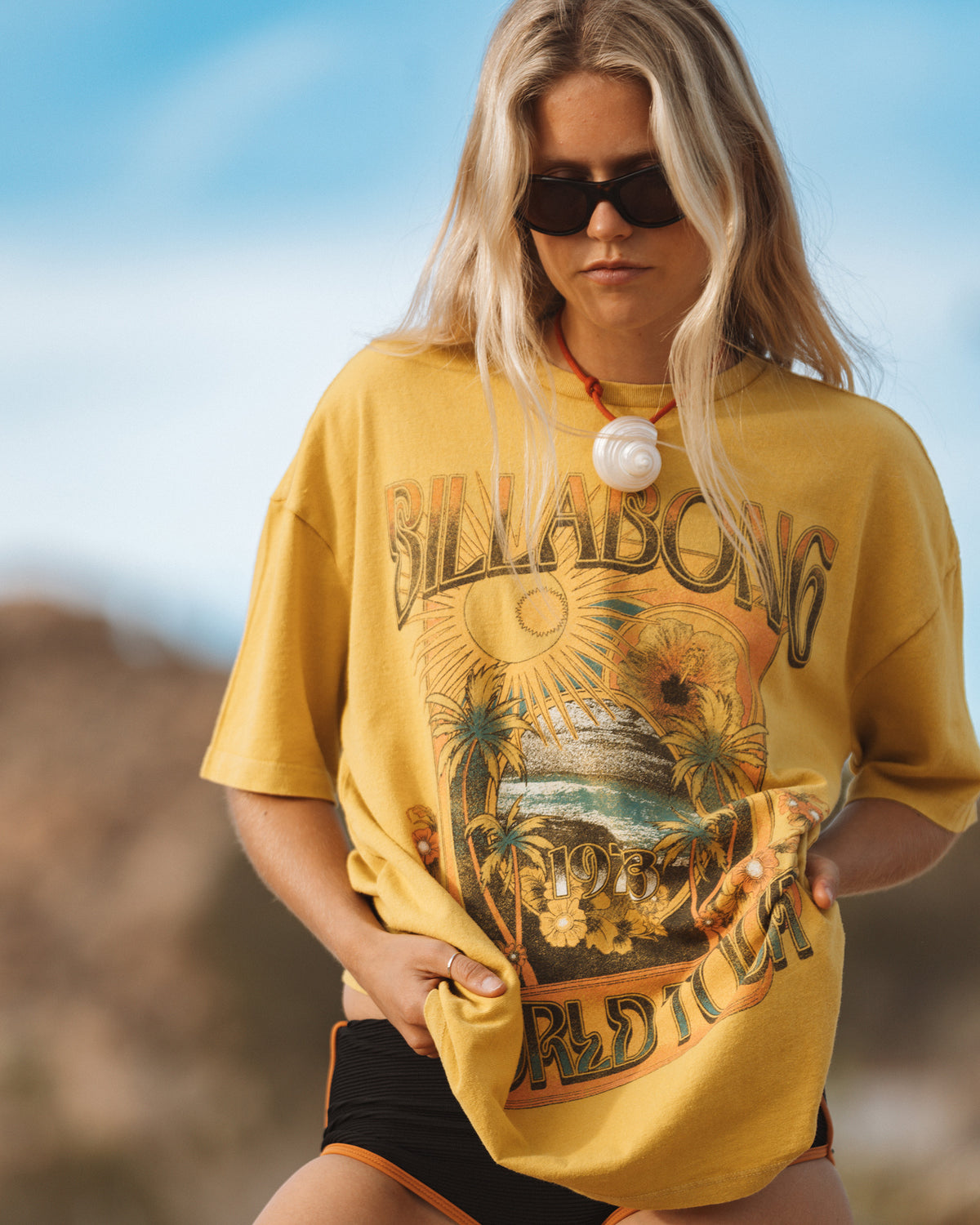 Dark citron short sleeve t-shirt with "Billabong" graphic featuring palm trees, sun, and ocean scene.