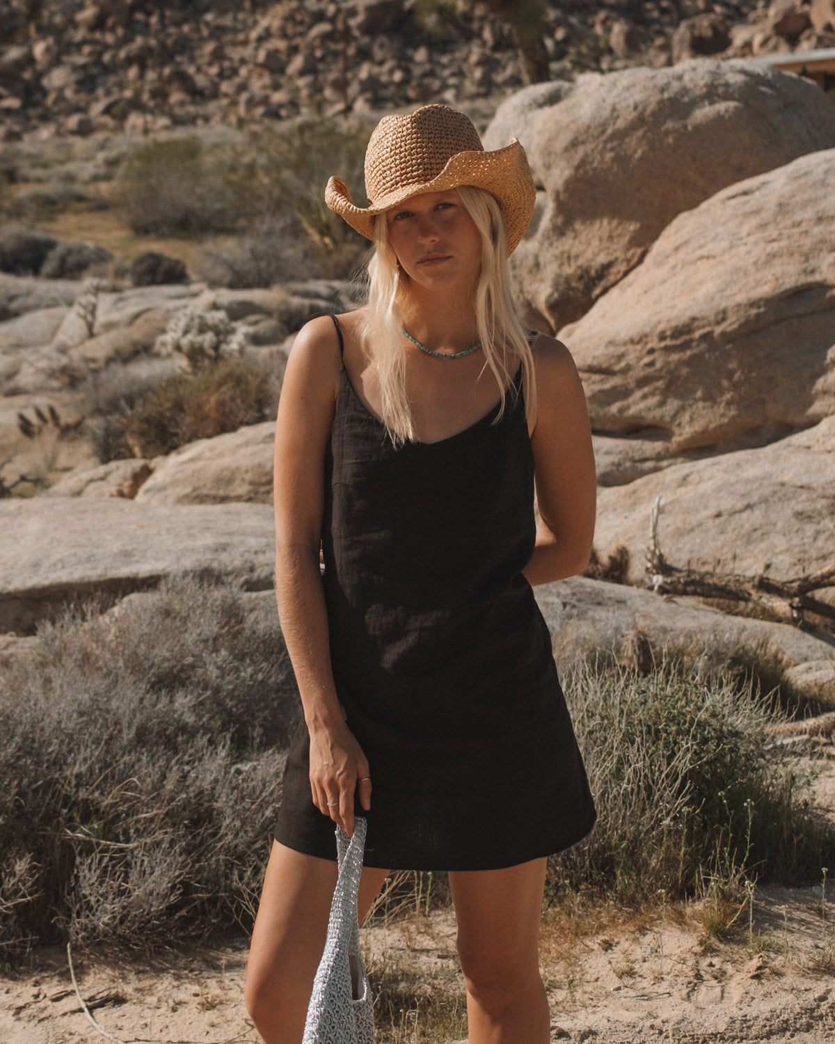 Tan woven cowboy hat with wide brim and curved crown worn by woman in desert setting.
