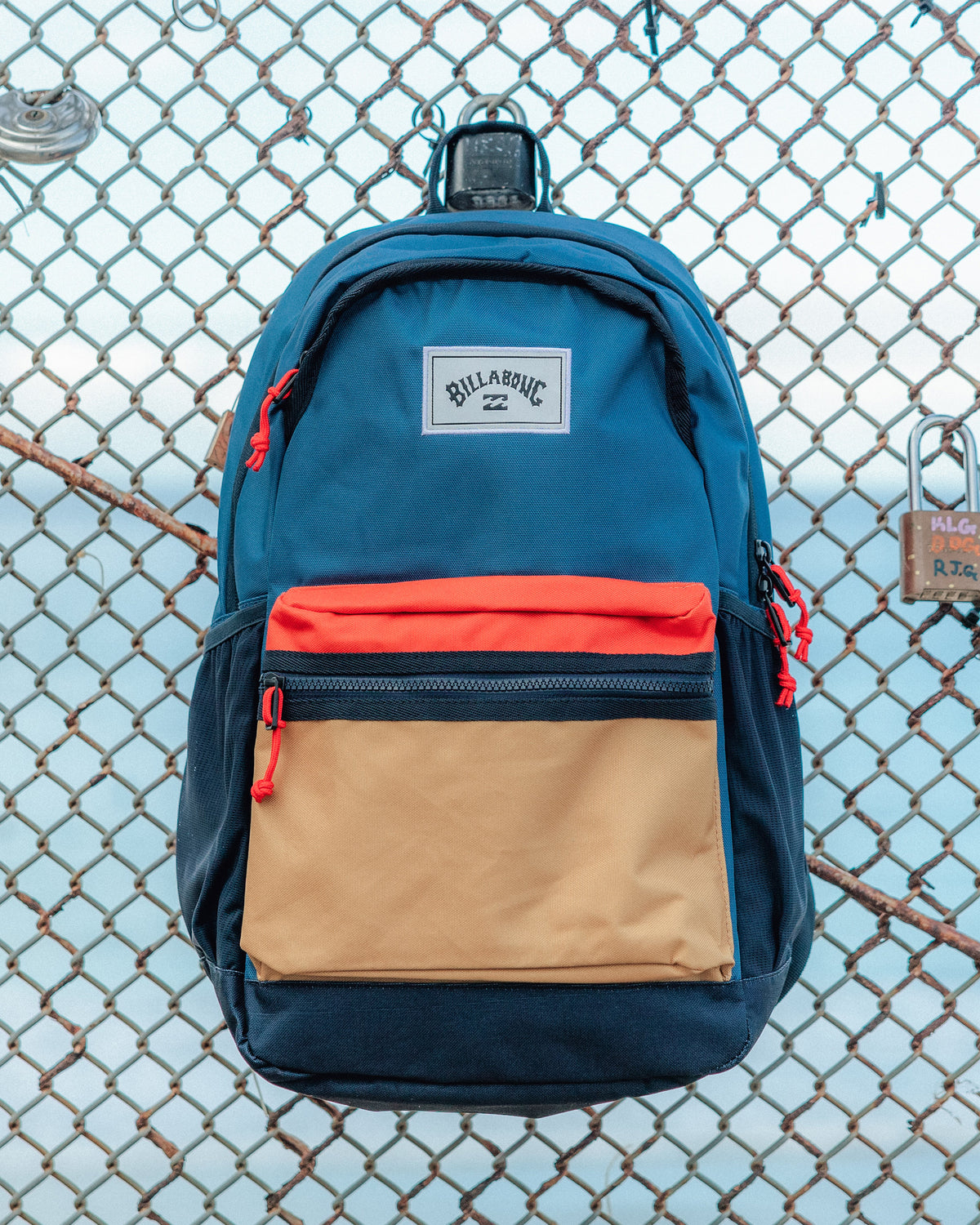 Blue, navy, orange, and tan colorblock backpack with front pocket and red zipper pulls.