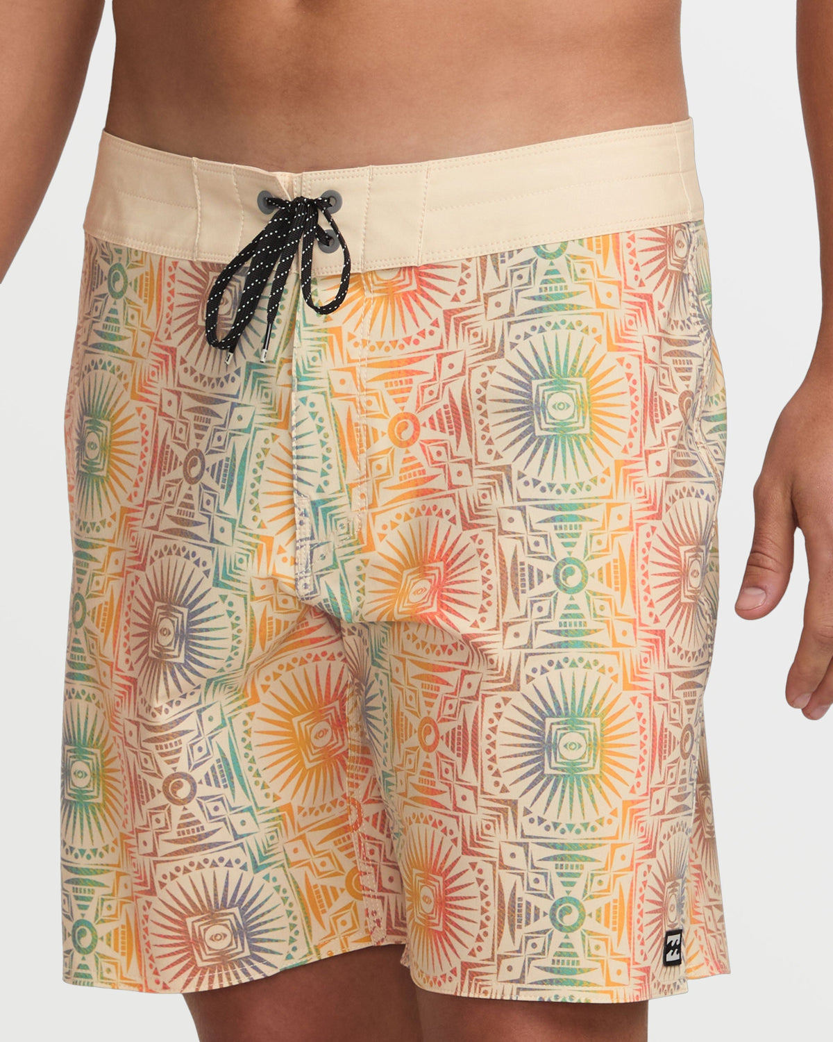 Tan boardshorts with geometric and sunburst pattern in orange, green, and red, black drawstring closure.