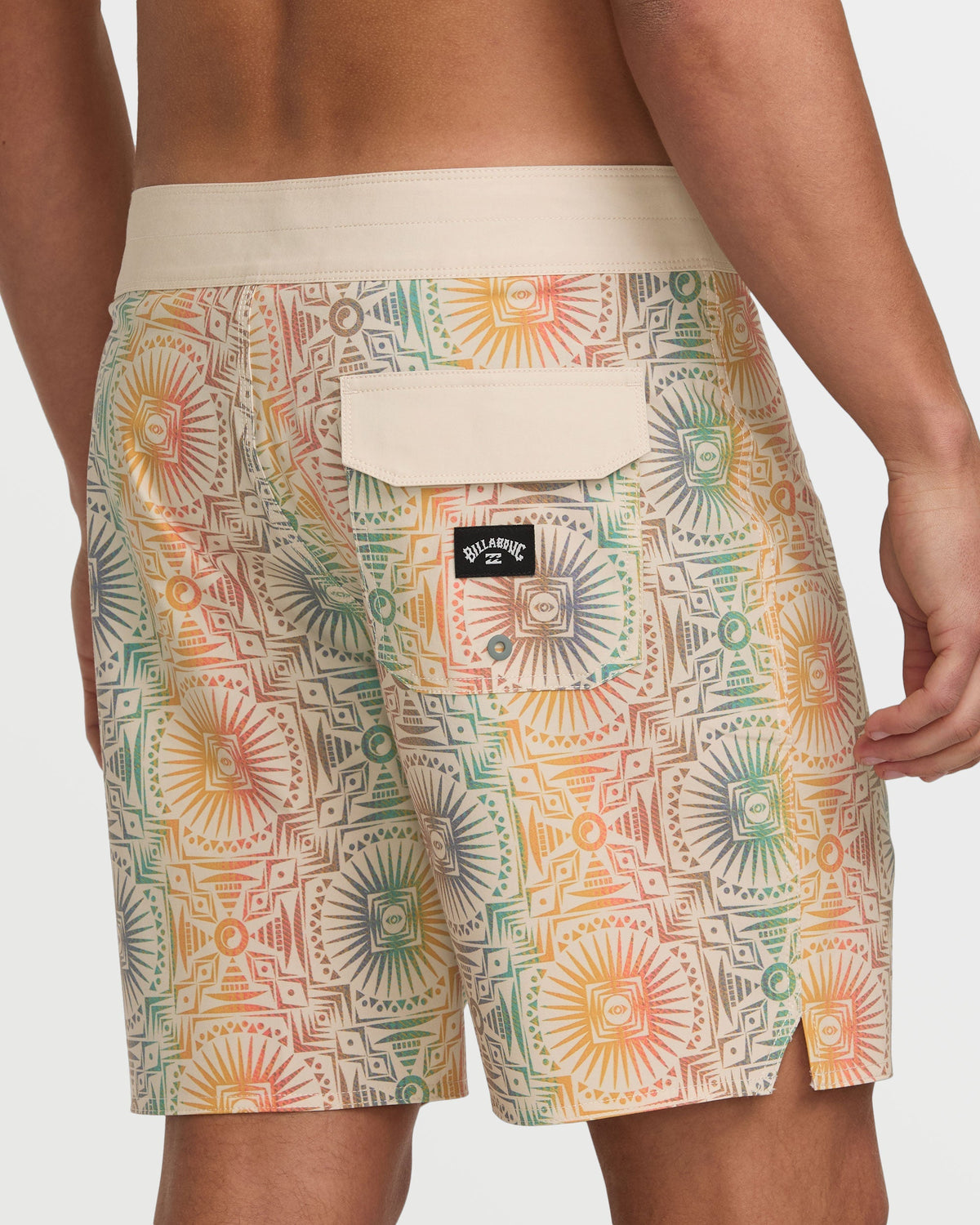 Tan boardshorts with geometric sunburst pattern in orange, green, and red, cream waistband, back pocket with Billabong logo.