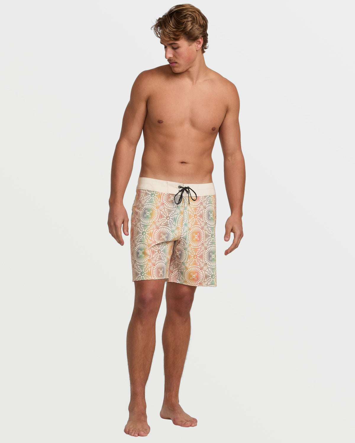 Man wearing tan boardshorts with multicolored circular geometric pattern and black drawstring waistband.