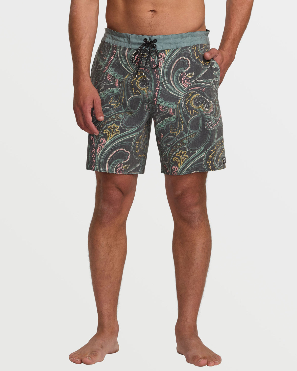Man wearing dark slate boardshorts with multicolored scrolling paisley pattern and blue waistband.