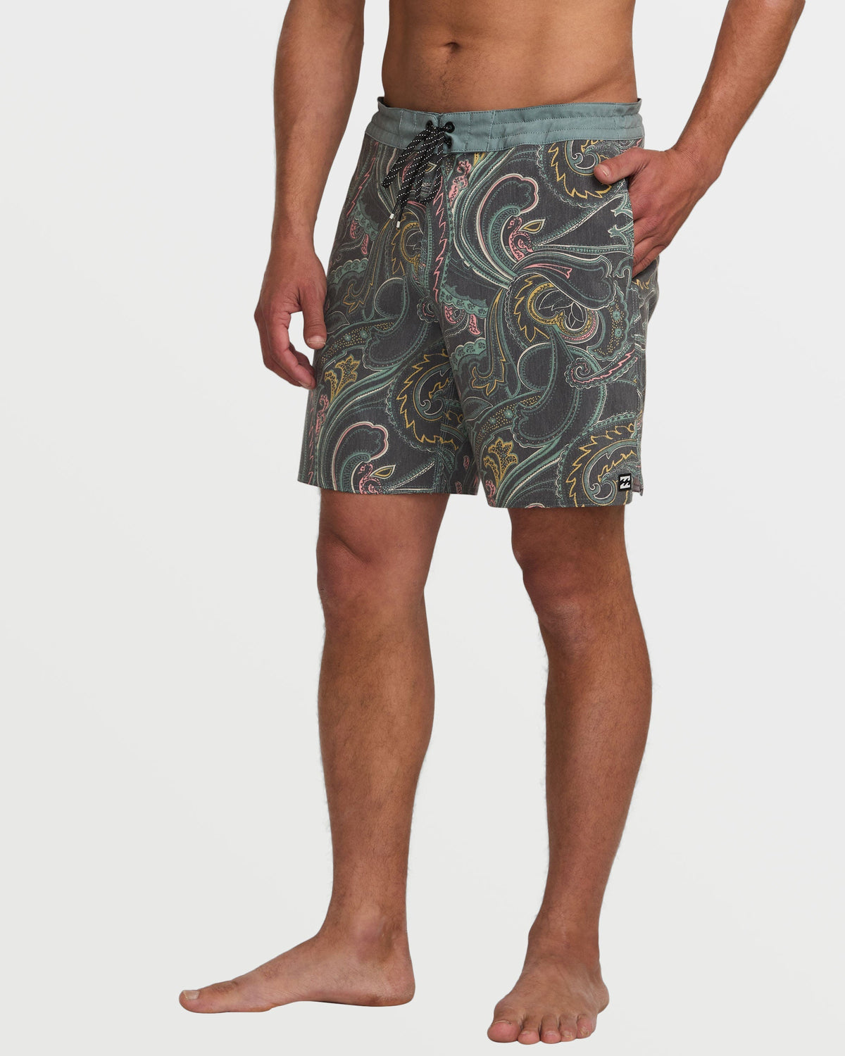 Man wearing dark slate boardshorts with ornate paisley and swirl pattern in gold, pink, and teal colors.