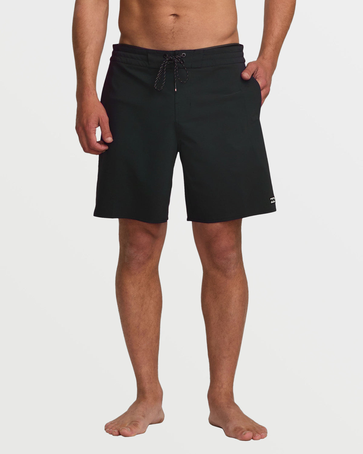 Black boardshorts with drawstring waist and side pockets worn by man standing barefoot.