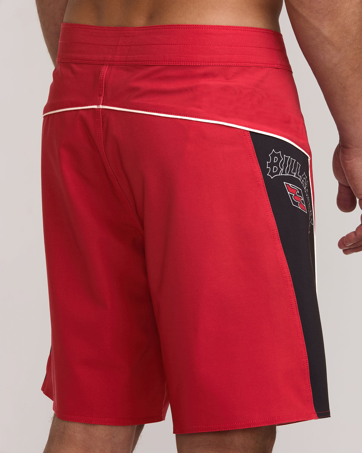 Red boardshorts with white stripe detail, black side panel with brand logo, and elastic waistband.