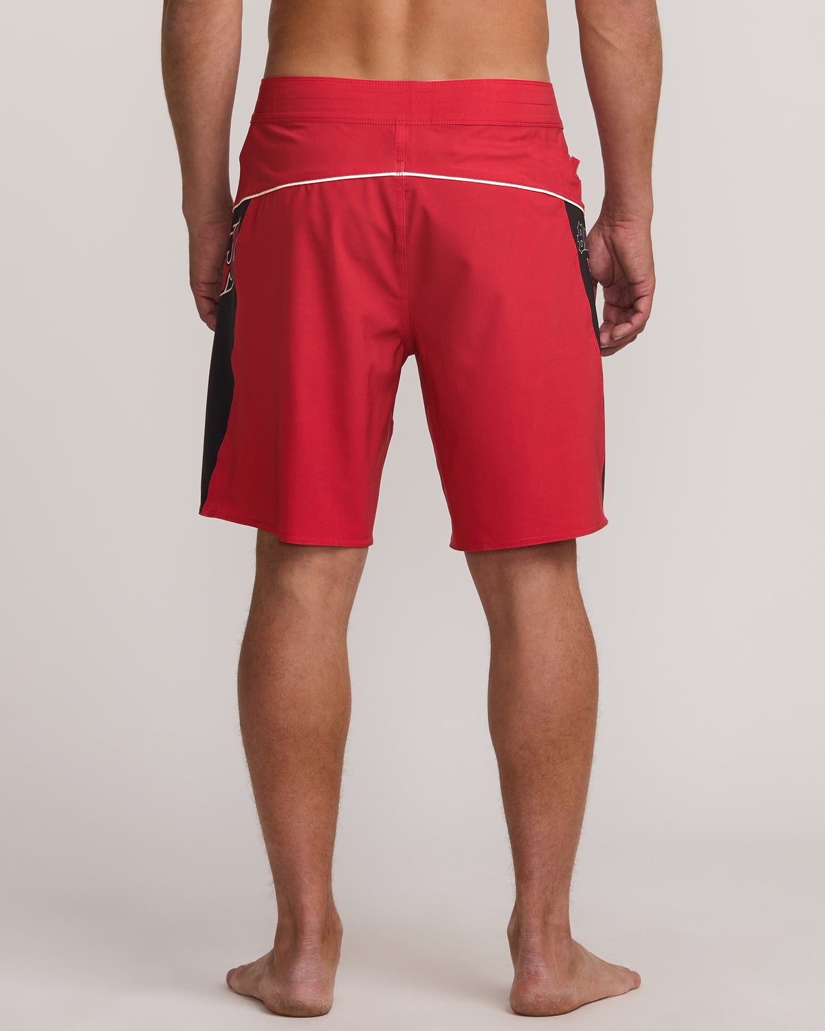Red boardshorts with black side panel and white waistband stripe, shown from back view.