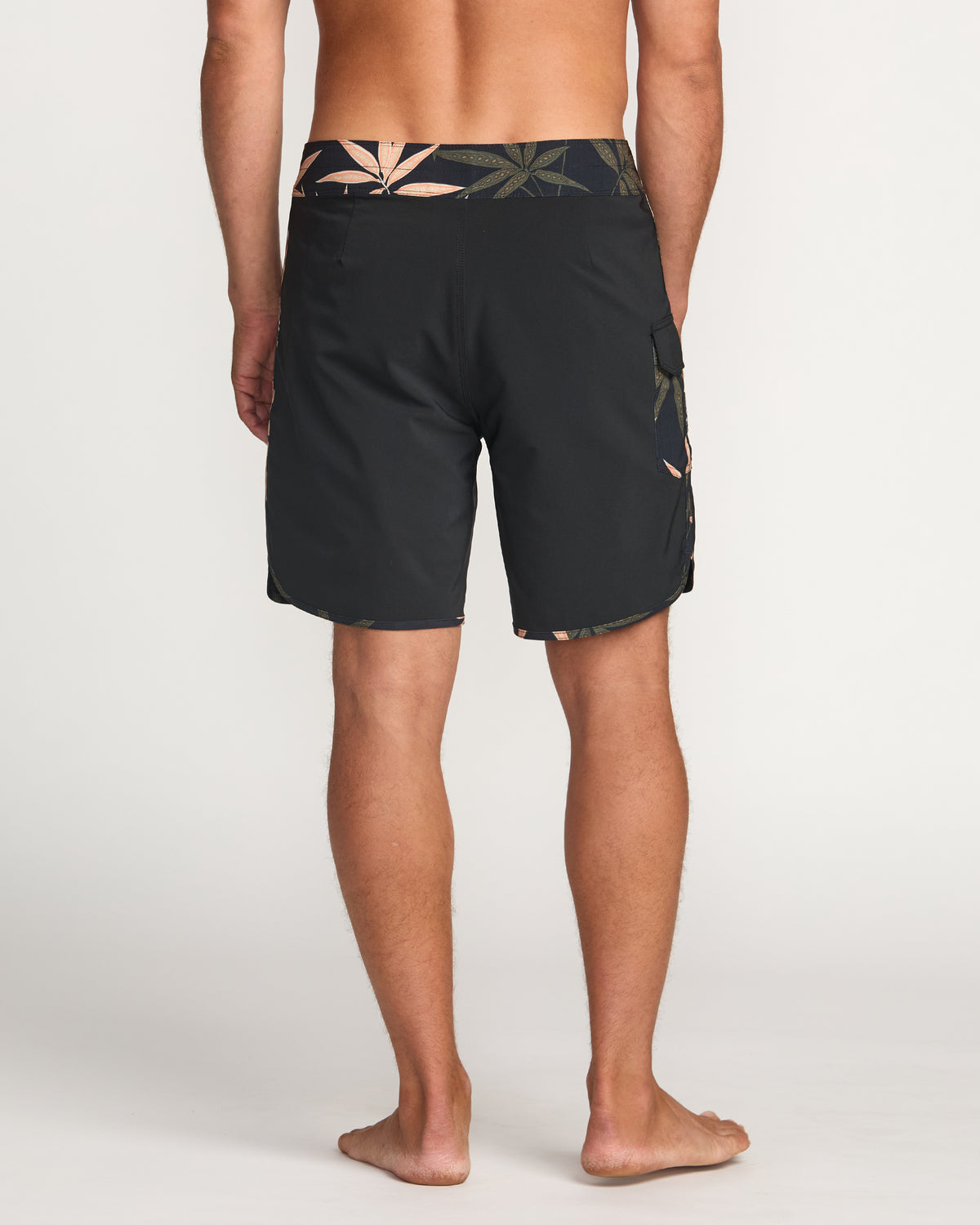 Man wearing black boardshorts with leaf pattern trim at waist and side pocket, rear view.