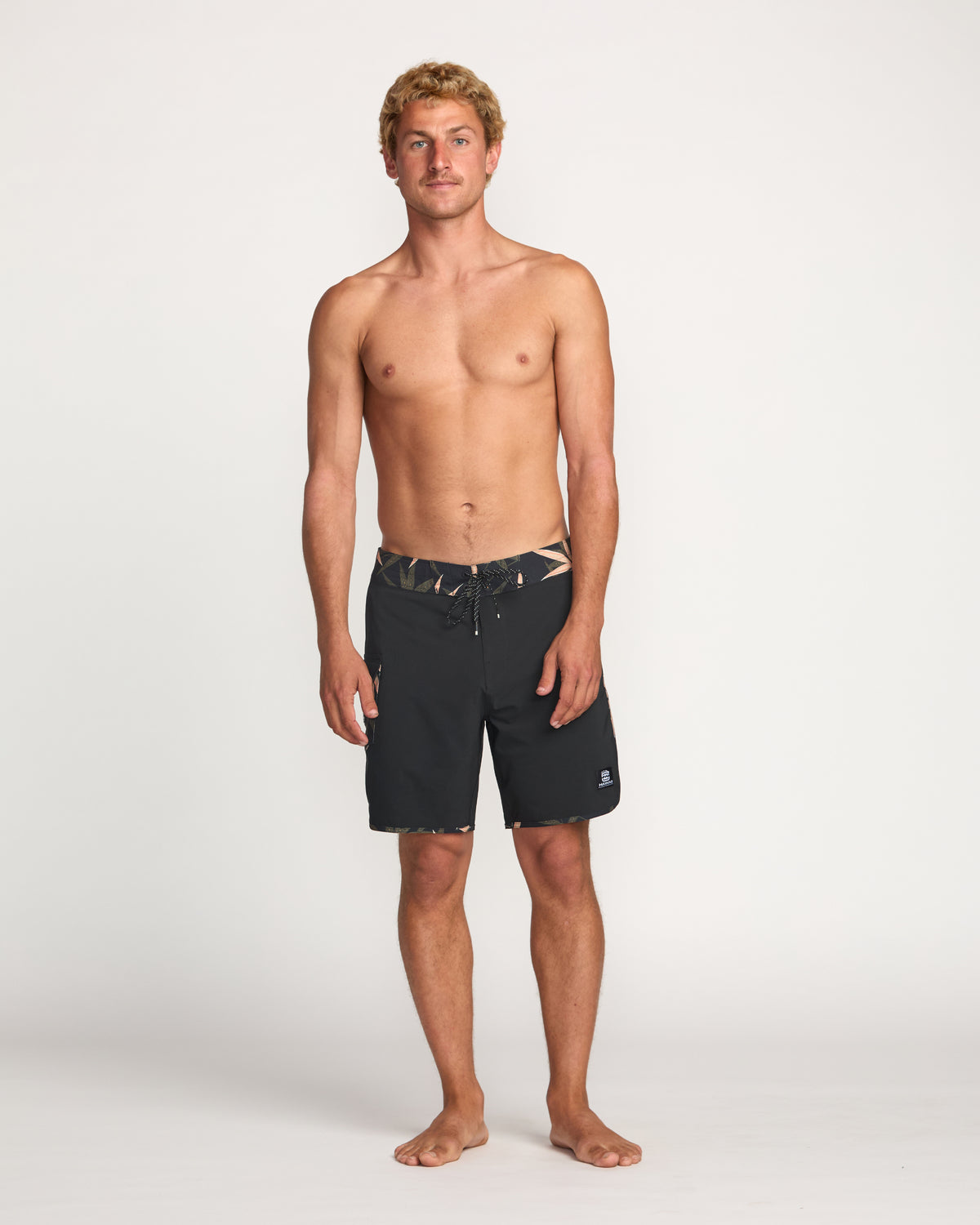 Man wearing black boardshorts with drawstring waistband and patterned trim detail.