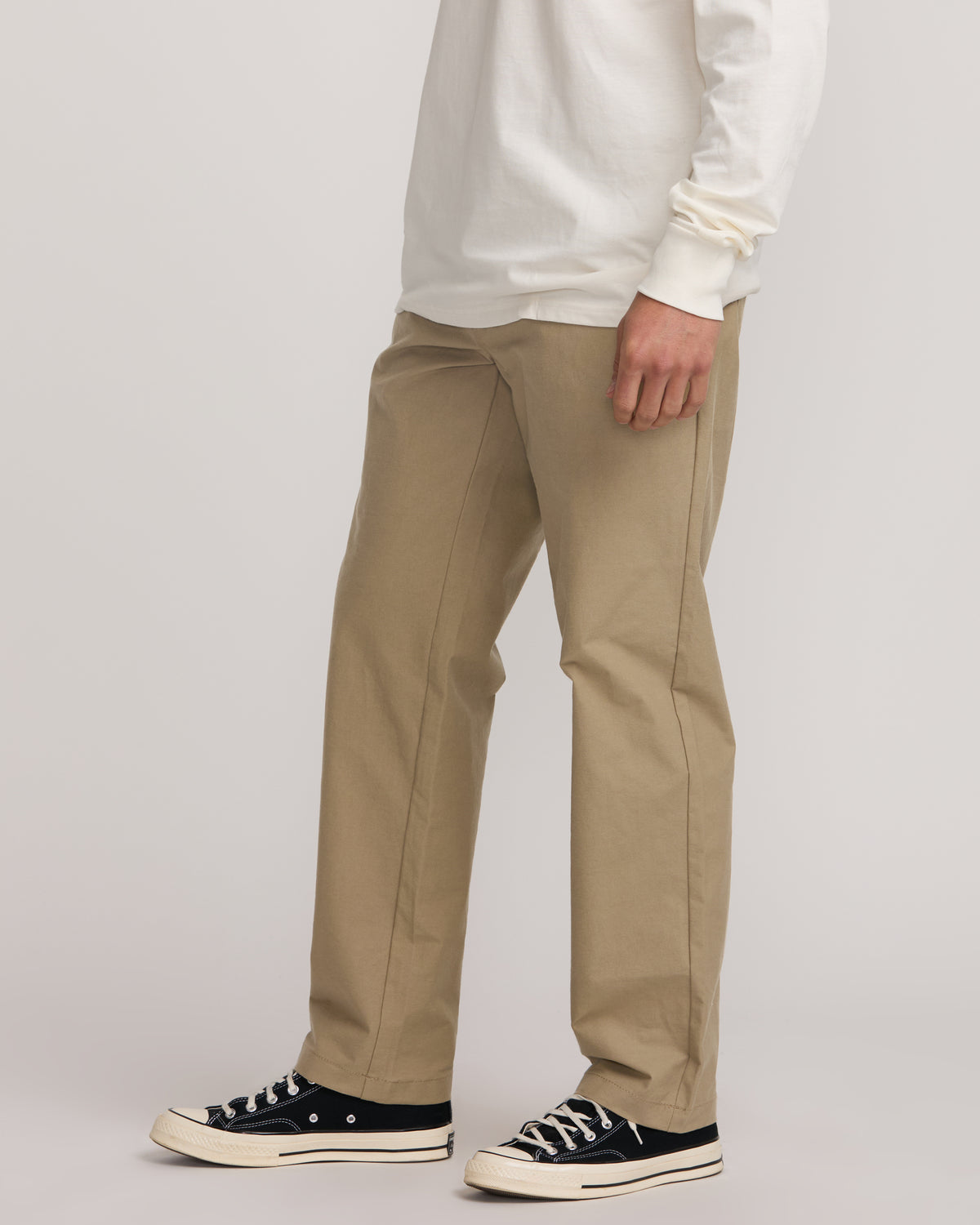 Gravel-colored straight-leg pants with flat front, worn with white long-sleeve shirt and black canvas sneakers.