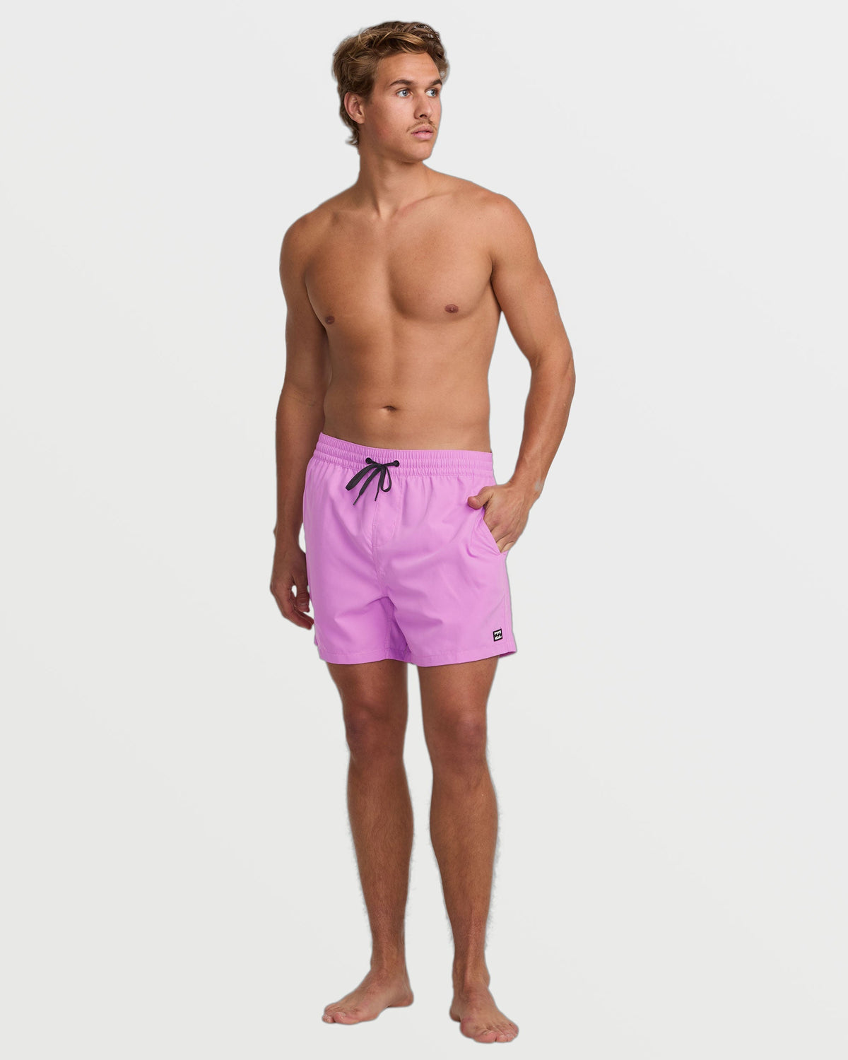 Man wearing fuchsia swim trunks with drawstring waist and side pockets.