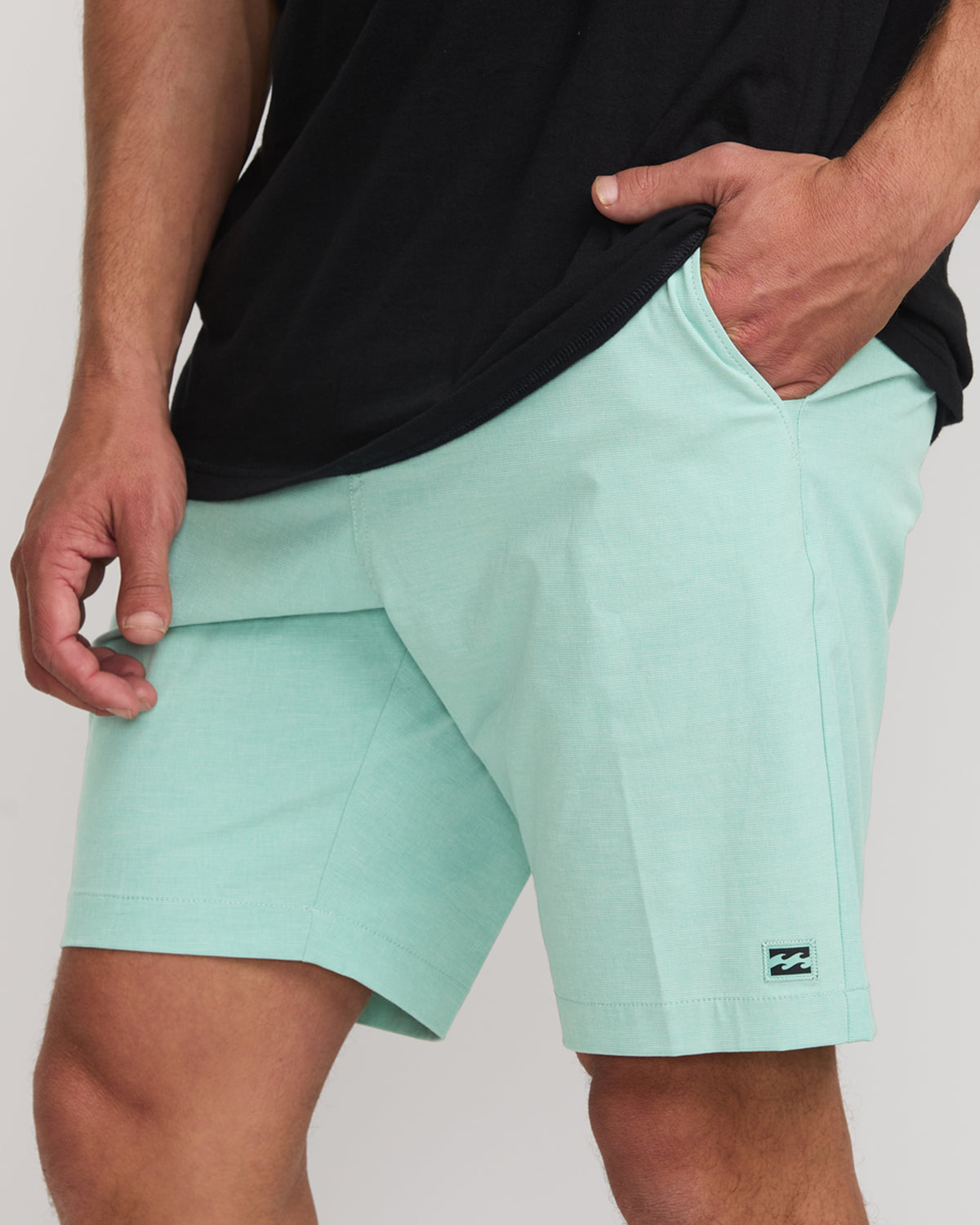 Man wearing light mint green hybrid shorts with black shirt, front pockets visible and small brand logo on leg.
