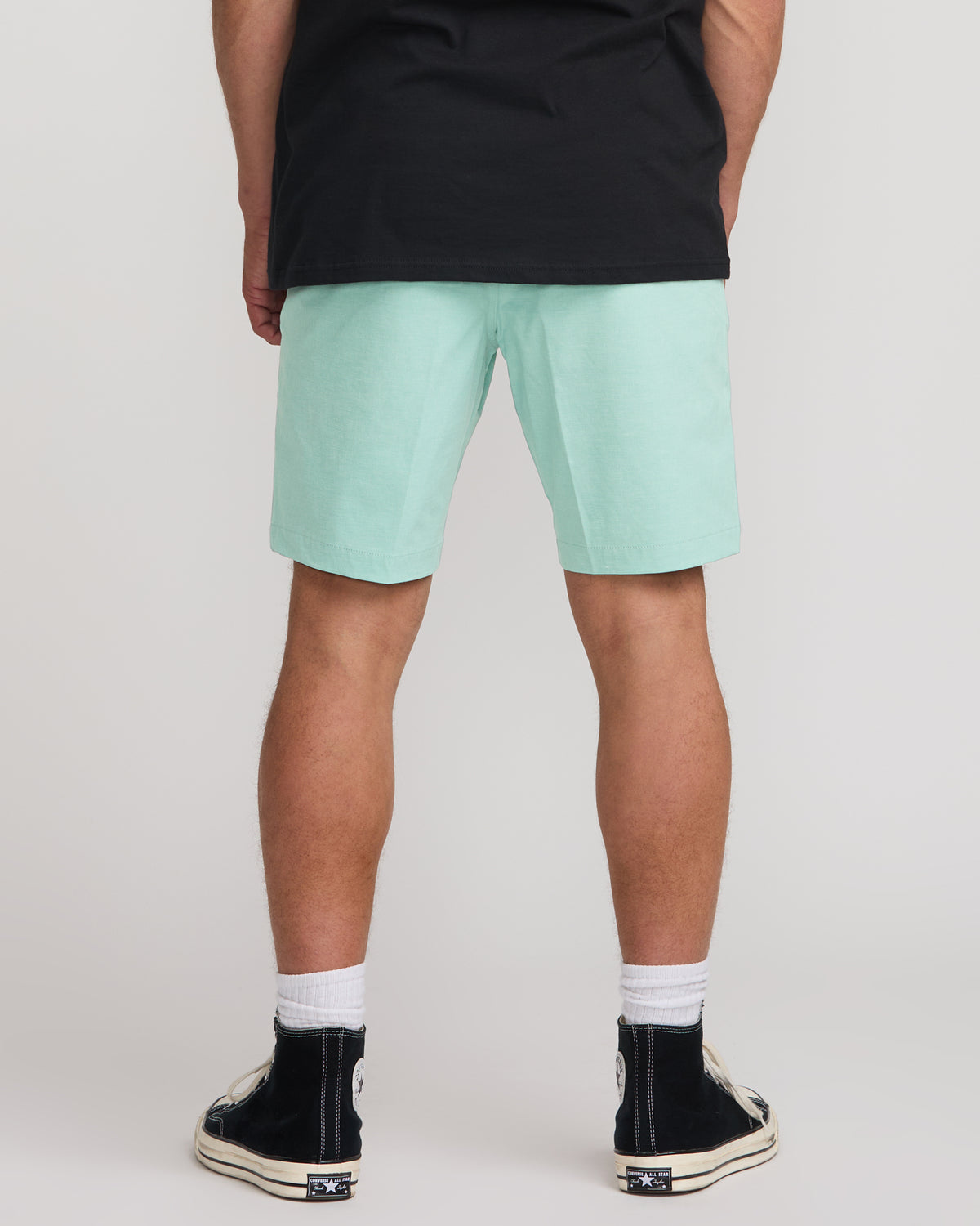 Man wearing mint green bermuda shorts with black t-shirt and black canvas sneakers.