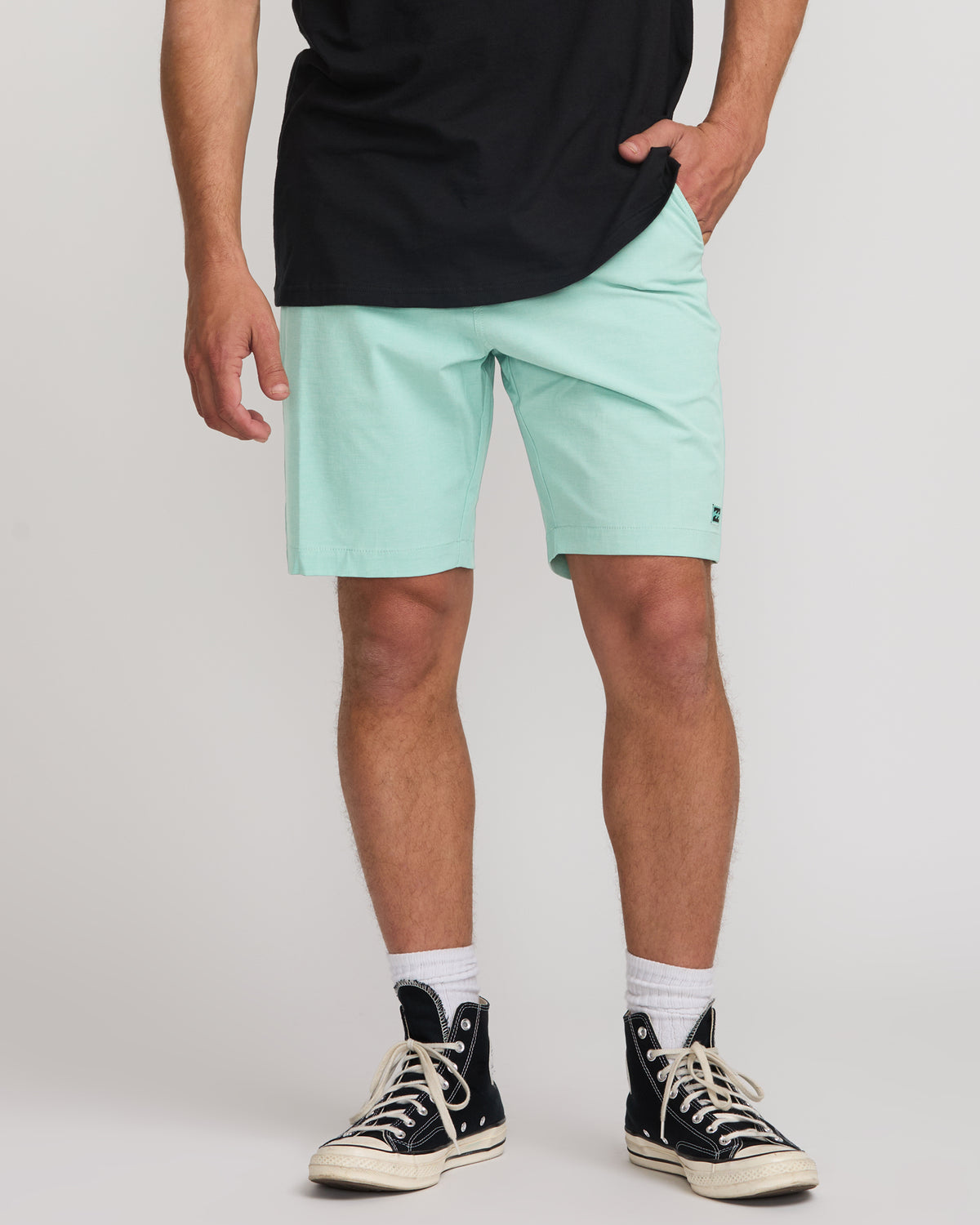 Man wearing mint green hybrid shorts with front pockets and small logo detail, paired with black shirt and black canvas sneak