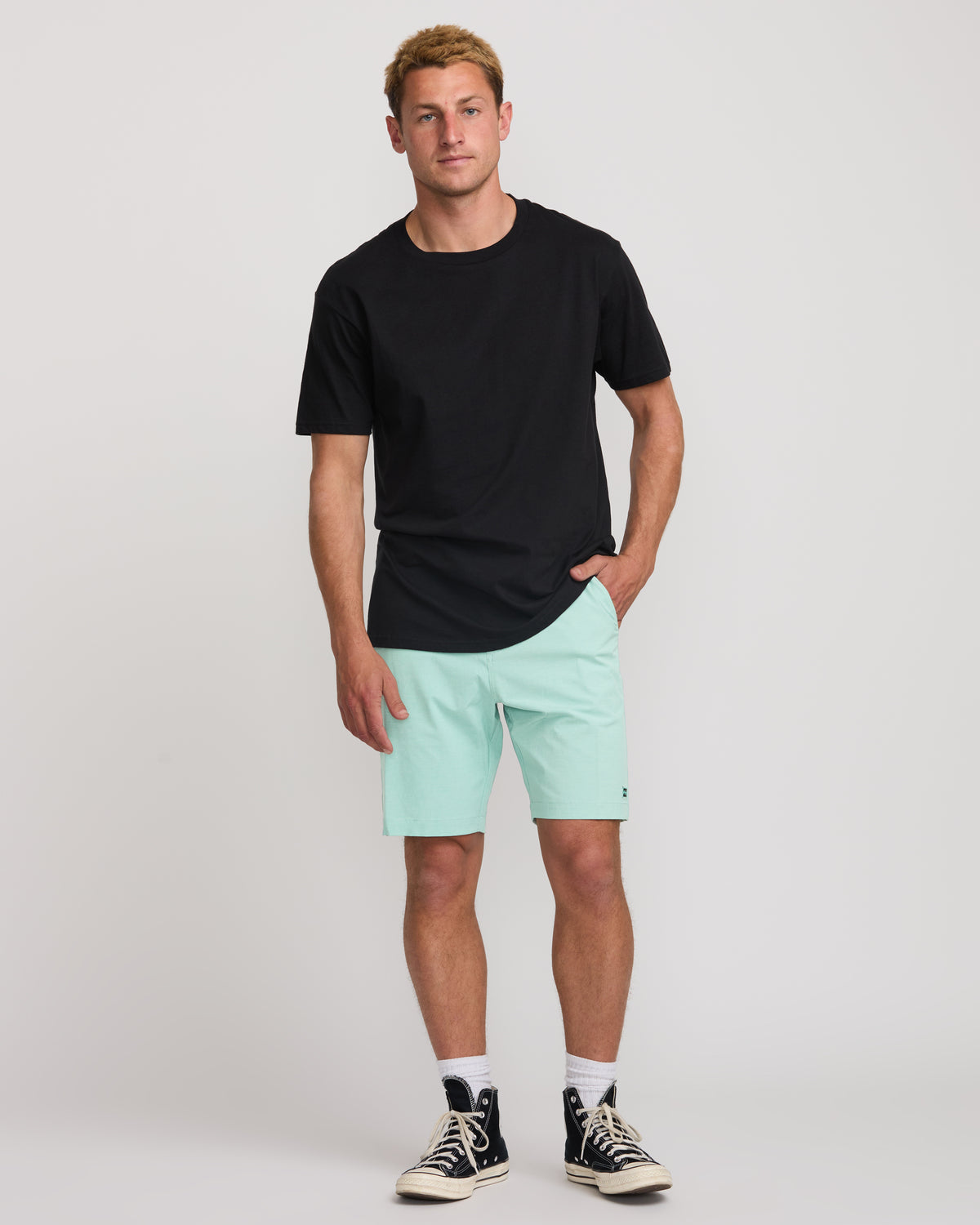 Man wearing black t-shirt and mint green bermuda shorts with front pockets, ending above the knee.