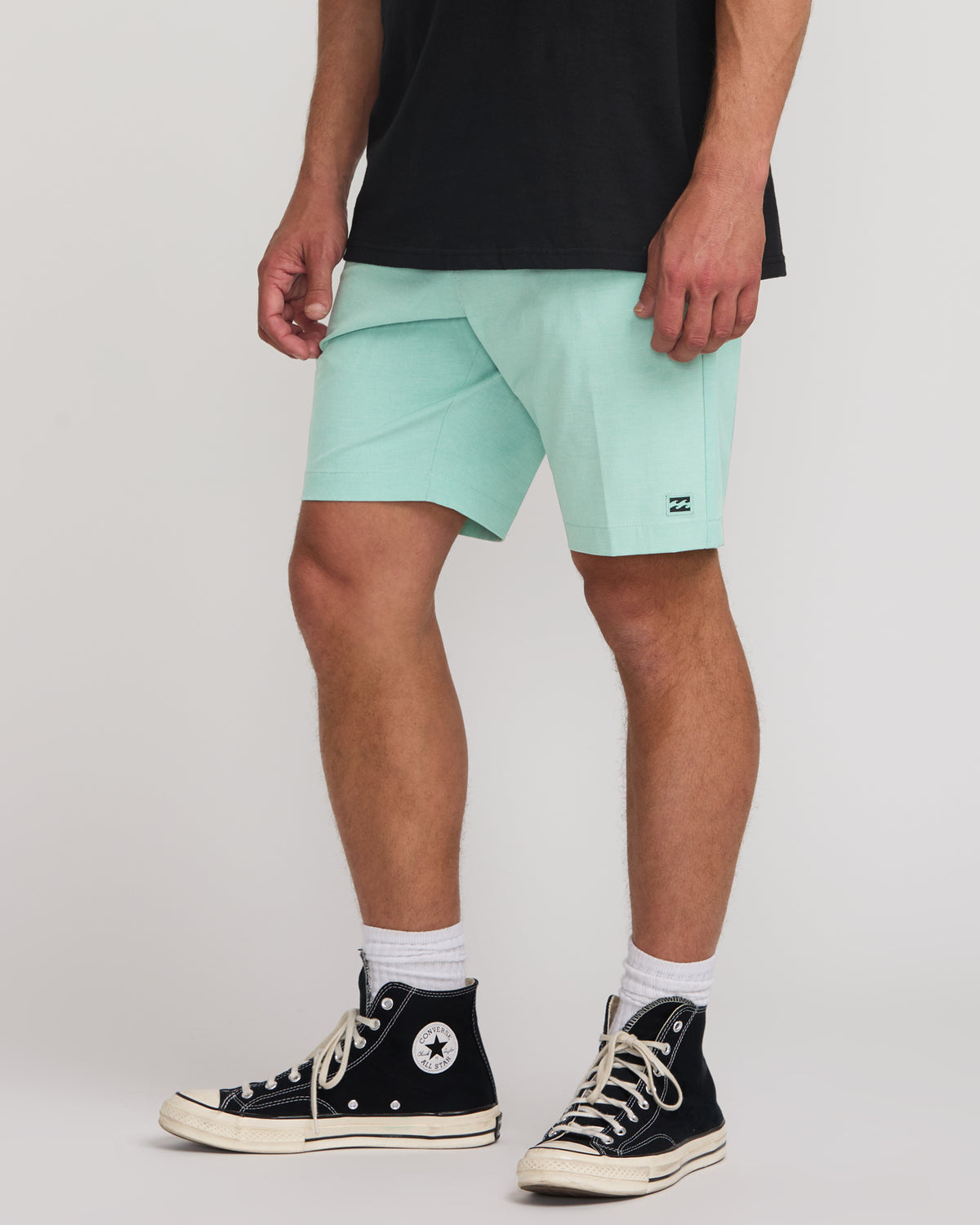 Man wearing mint green hybrid shorts with black logo patch, paired with black and white high-top sneakers.