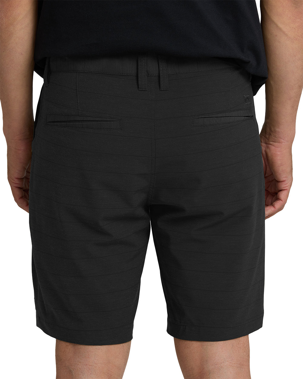 Black hybrid shorts with flat front, belt loops, and back flap pockets, shown from behind on a model.