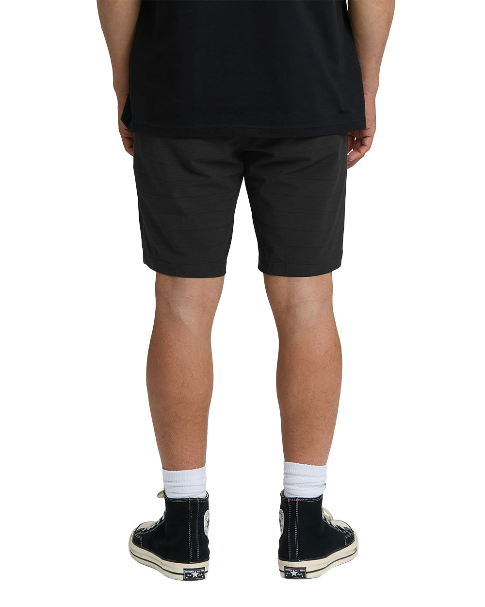 Black hybrid shorts on person wearing white socks and black sneakers, rear view.