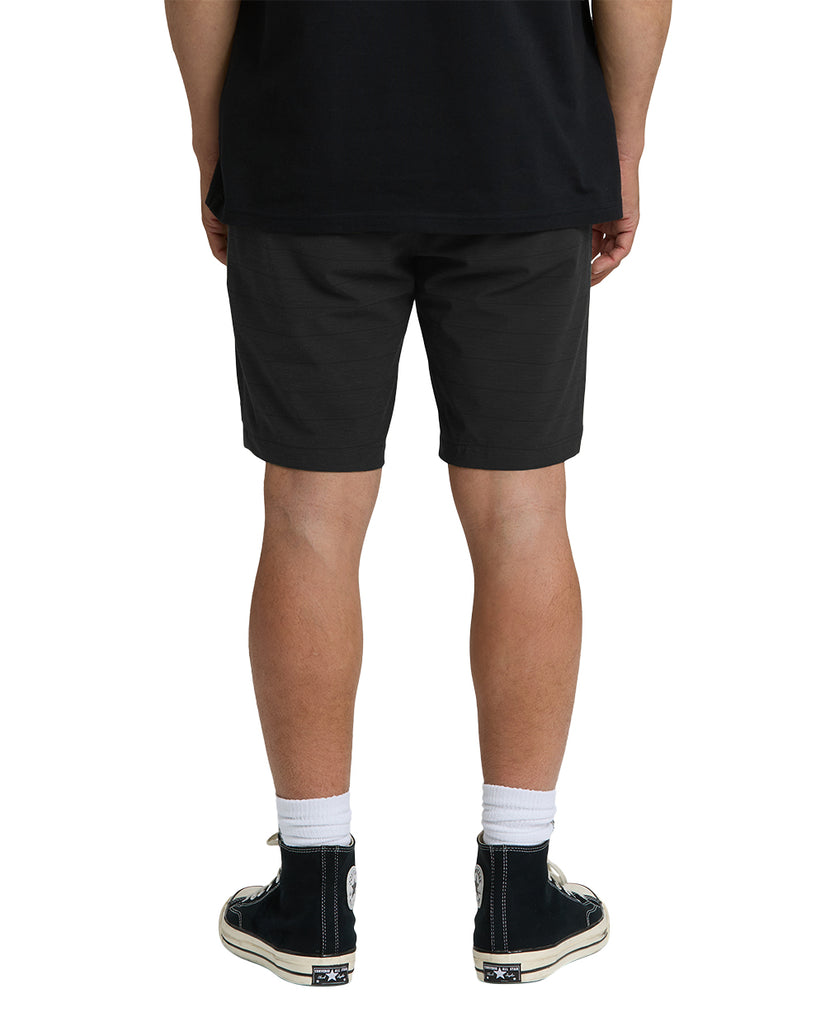 Black hybrid shorts on person wearing white socks and black sneakers, rear view.