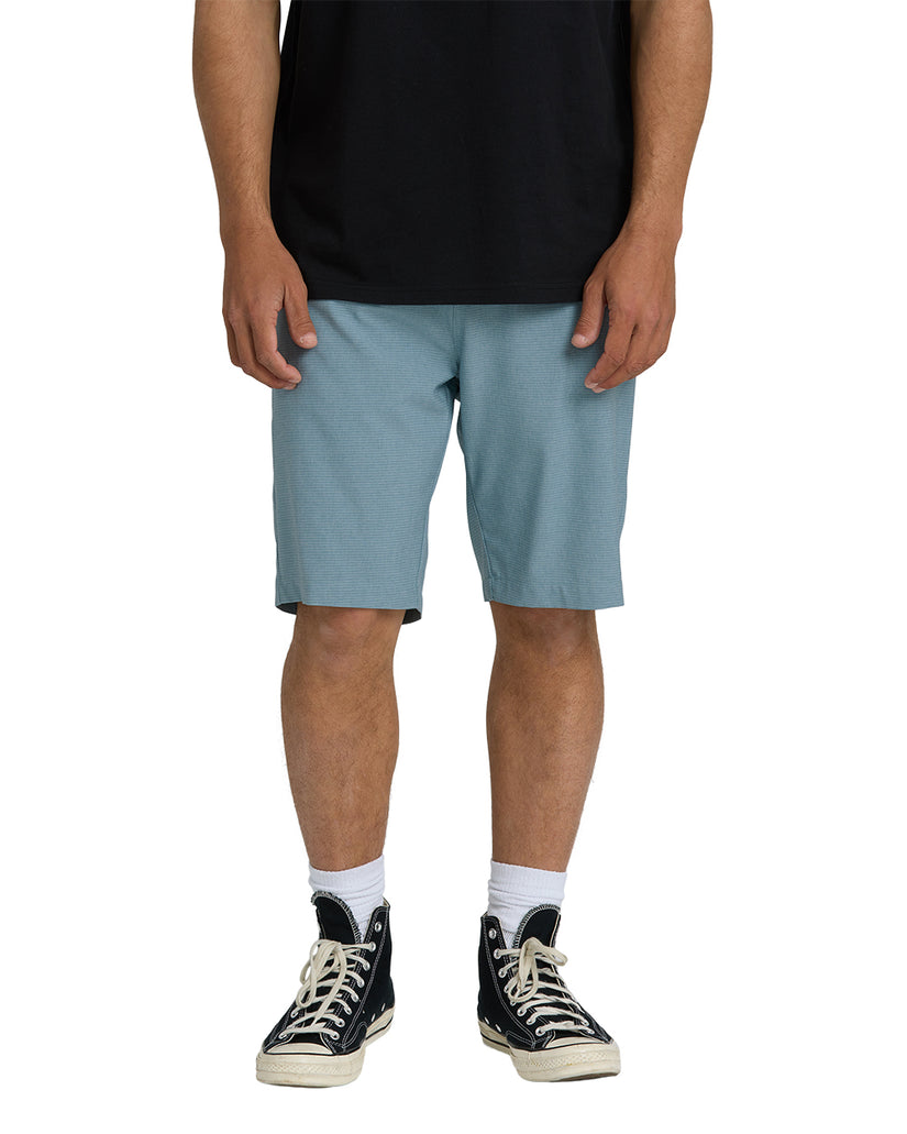 Man wearing light blue textured hybrid shorts with black shirt and black canvas high-top sneakers.
