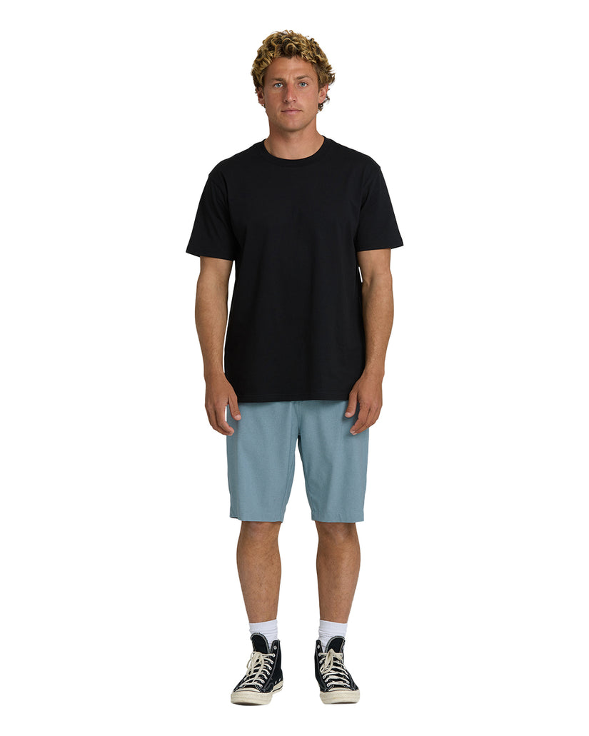 Man wearing black t-shirt and blue fog hybrid shorts with white socks and black canvas sneakers.