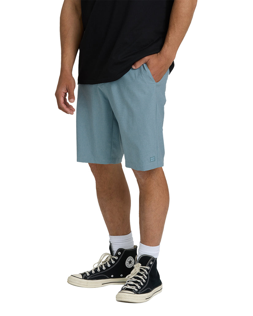 Men's blue-gray hybrid shorts with front pockets and textured fabric, worn with black t-shirt and black high-top sneakers.