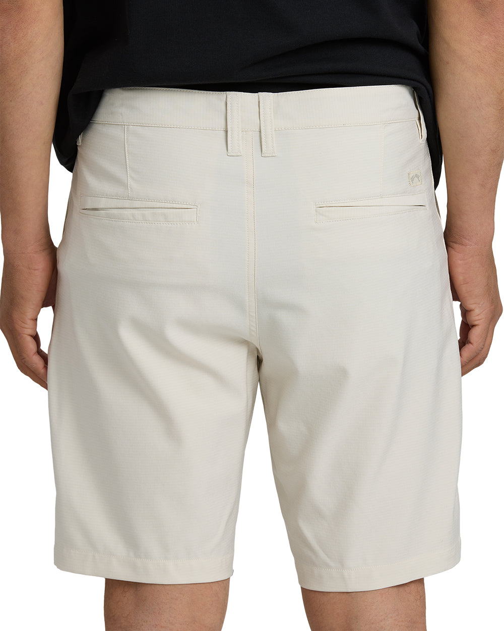 Oatmeal-colored hybrid shorts with flat front, drawstring waistband, and flap pockets, worn with black shirt.