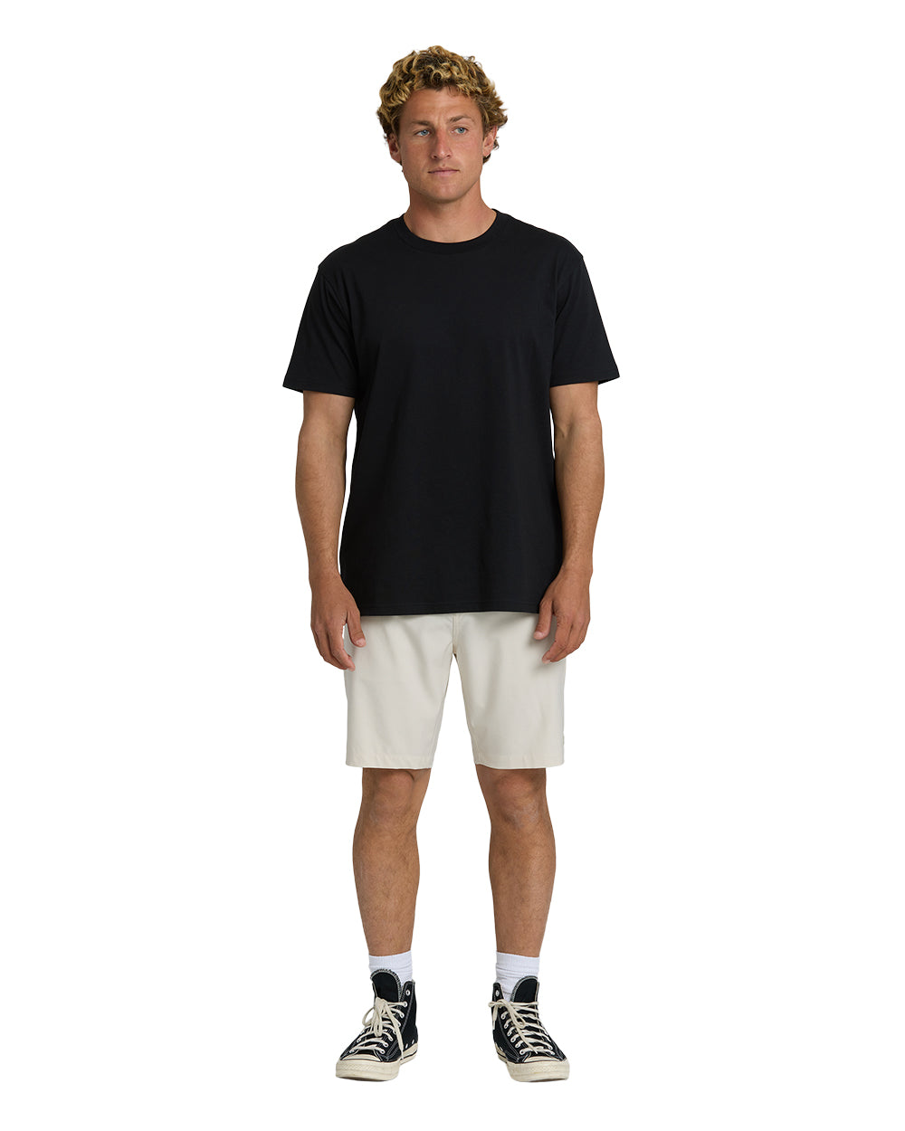 Man wearing black short-sleeve t-shirt and oatmeal-colored 19-inch hybrid shorts with white socks and black canvas sneakers.