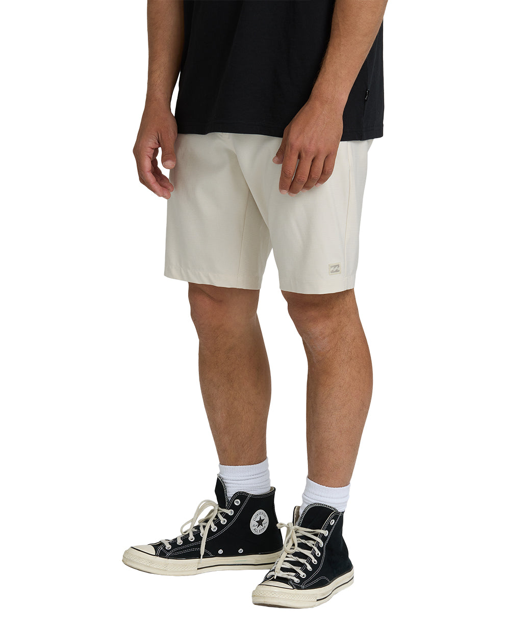 Oatmeal hybrid shorts with drawstring waist and side pockets, worn with black shirt and black canvas high-top sneakers.