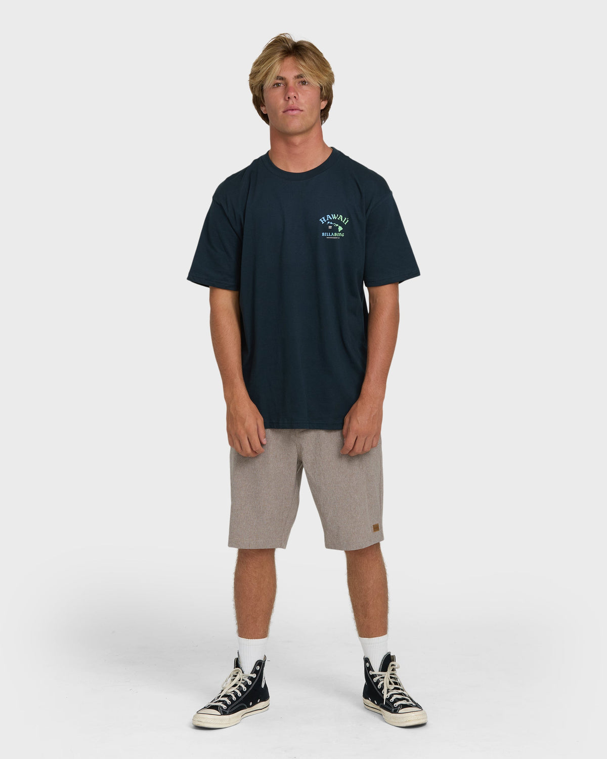Navy short sleeve t-shirt with small chest graphic, worn with gray shorts and black canvas sneakers.