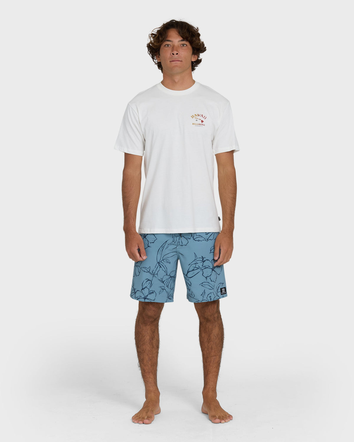 Off-white short-sleeve tee with small Hawaii graphic on chest, worn with blue patterned shorts.