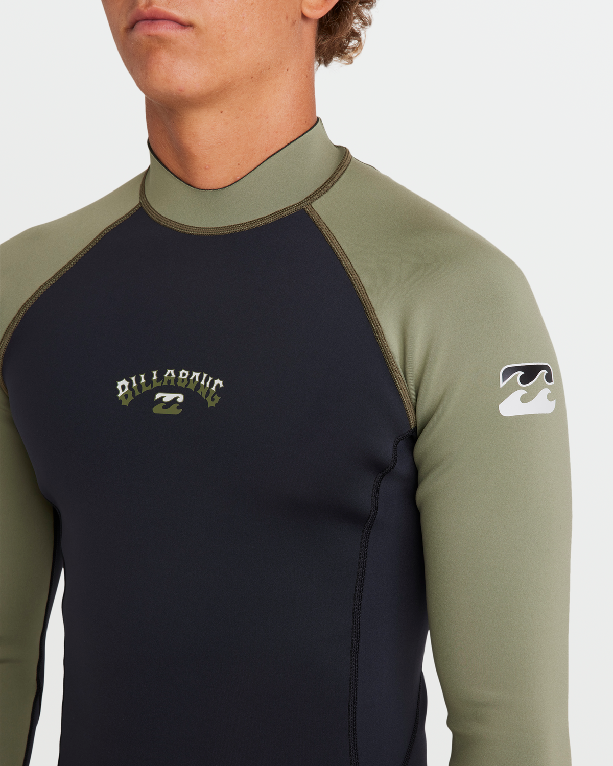 Man wearing long sleeve wetsuit jacket with black front panel and sage green sleeves, featuring contrasting stitching and bra