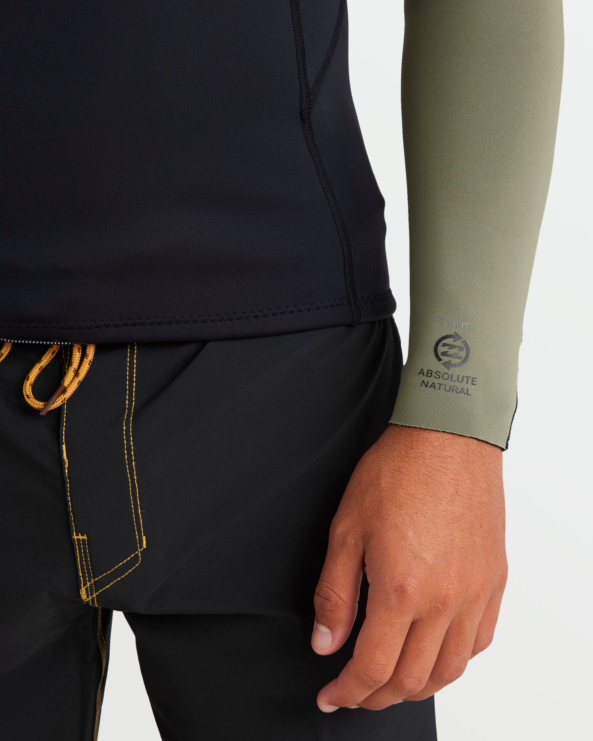 Olive green long sleeve wetsuit jacket with "Absolute Natural" branding on the cuff, worn with black shorts with orange draws