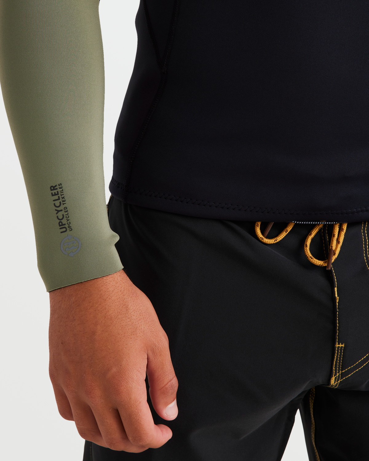 Sage green long sleeve jacket sleeve with "Upcycler" branding worn over black pants with gold stitching detail.
