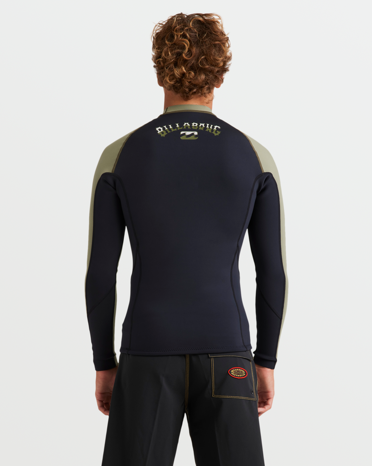 Man wearing black and olive long-sleeve wetsuit jacket with Billabong branding on back, shown from behind.