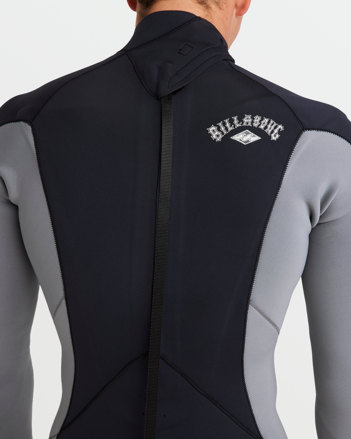 Man wearing black and gray fullsuit wetsuit with back zip closure and Billabong branding on back.