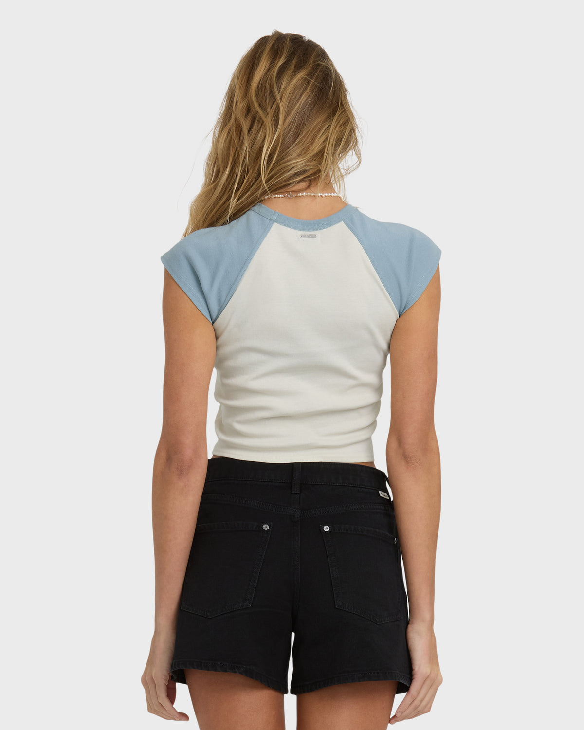 Short sleeve raglan tee with mineral blue sleeves and cream body, worn with black denim shorts.