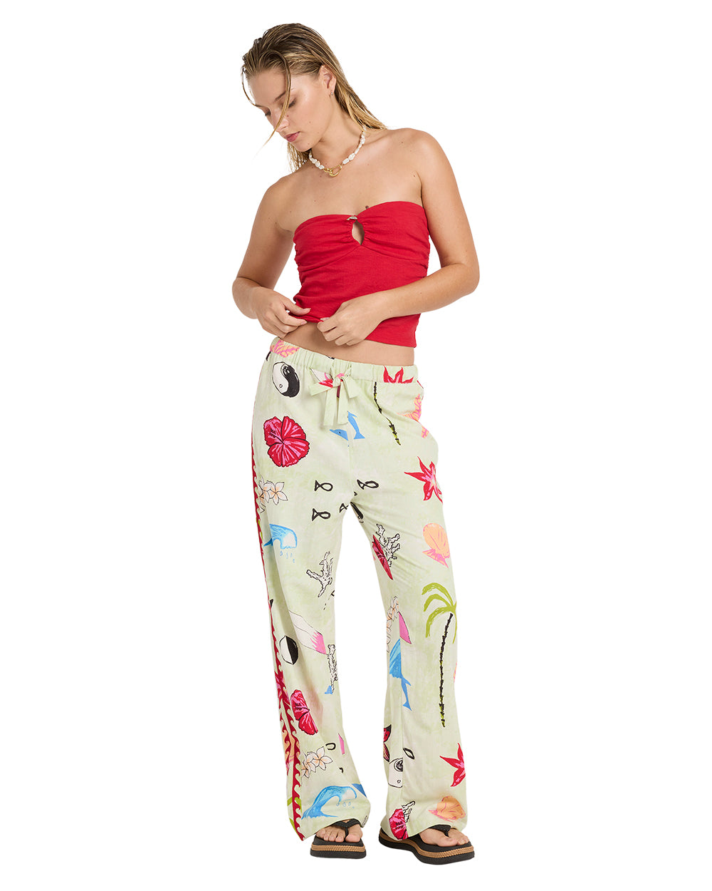 Woman wearing a true red strapless tube top with a cutout detail and cream pants with colorful floral print.