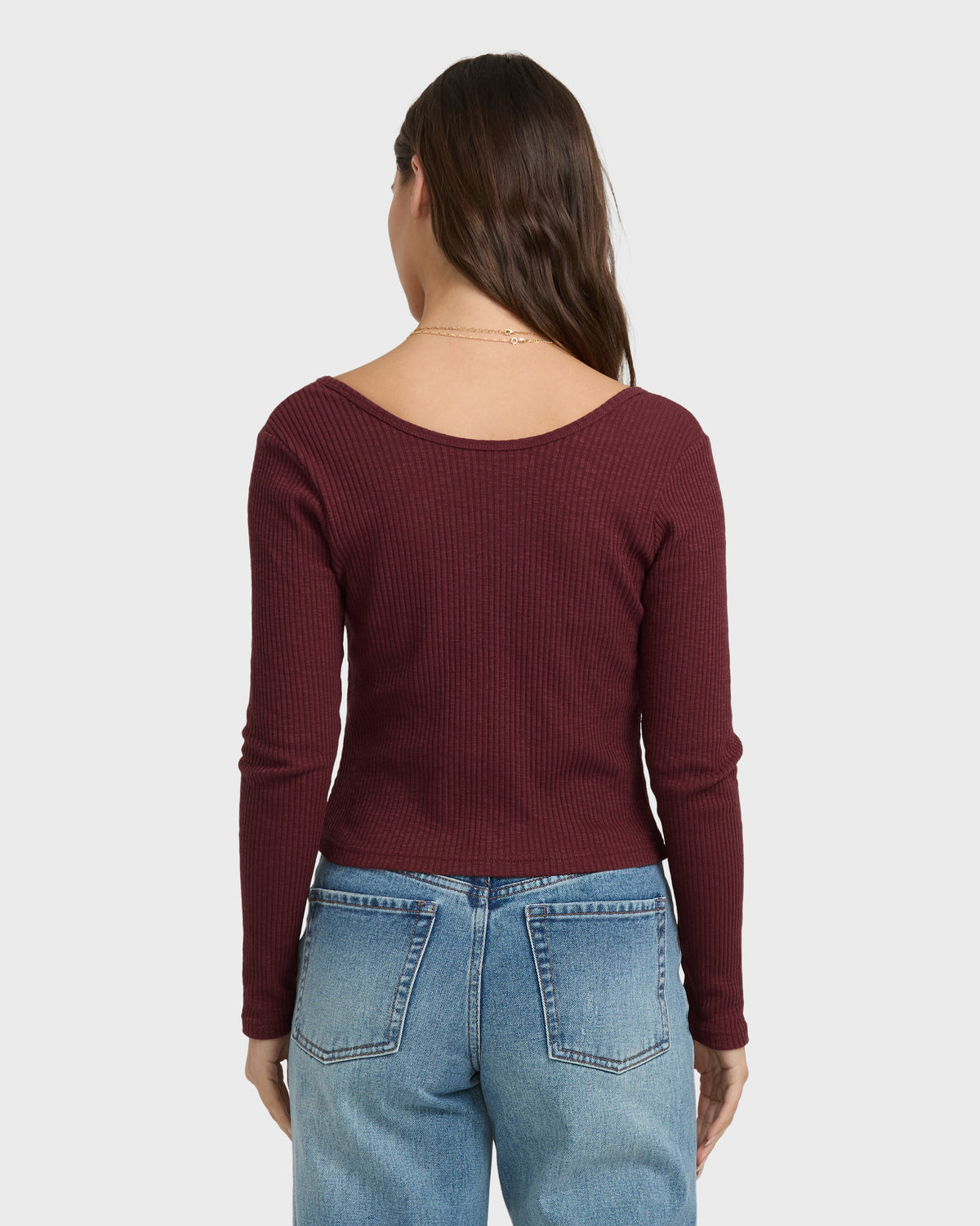Burgundy ribbed long-sleeve knit top with twisted front detail, shown on model with light blue jeans.
