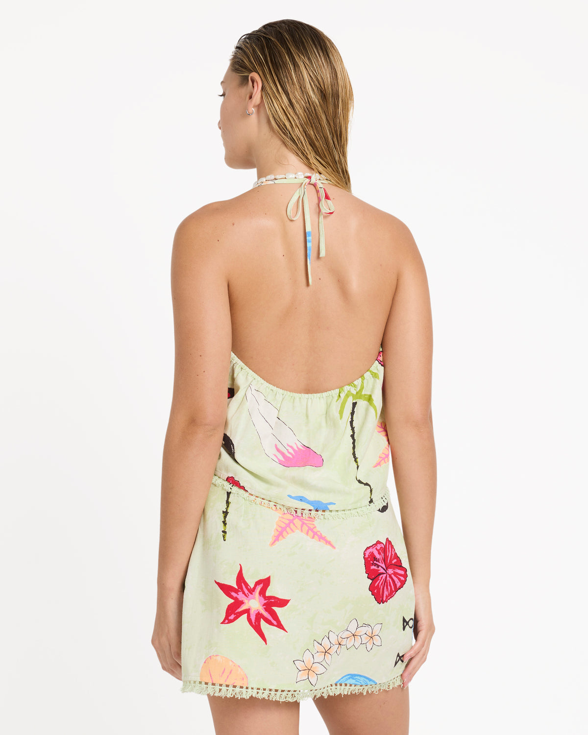 Woman wearing a lime green sleeveless woven tank dress with colorful floral and botanical print, halter neckline, and decorat
