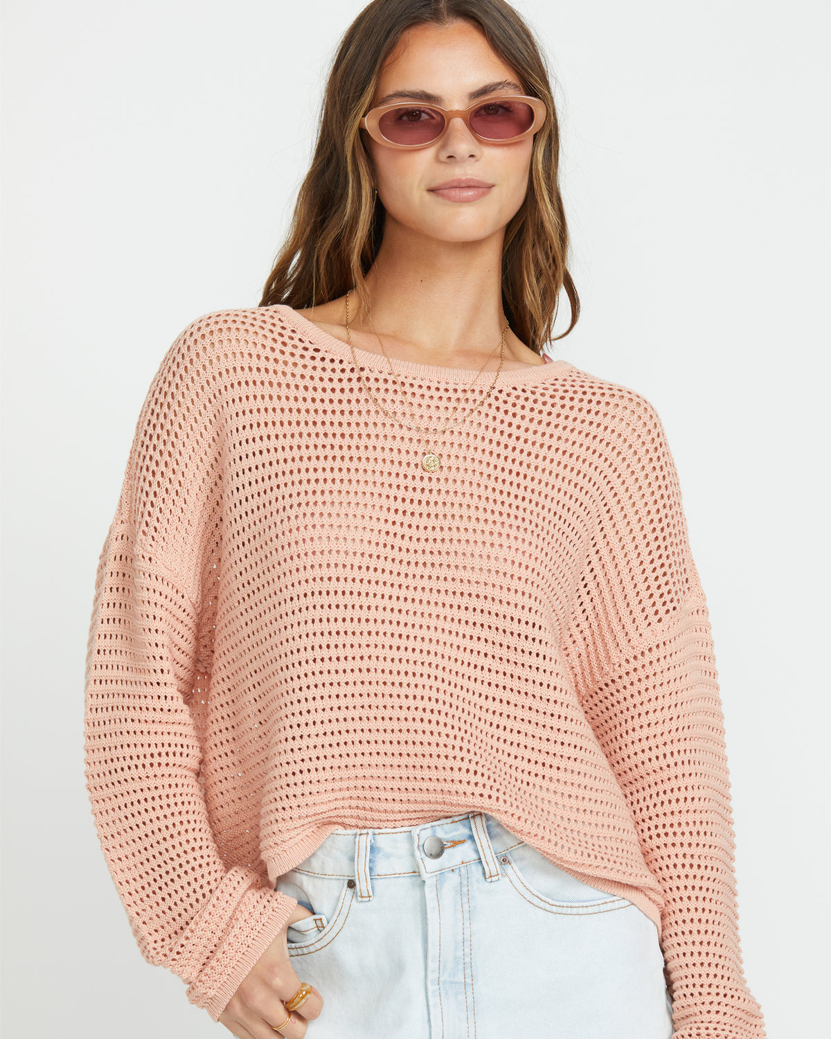 Faded rose open-knit crewneck sweater with long sleeves on model wearing light wash jeans.