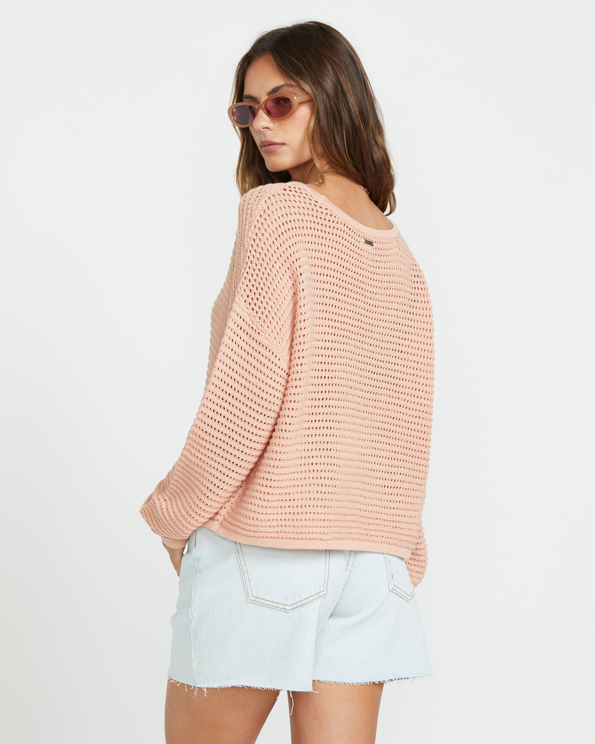 Faded rose knit sweater with open stitch pattern and long sleeves worn with light denim shorts.