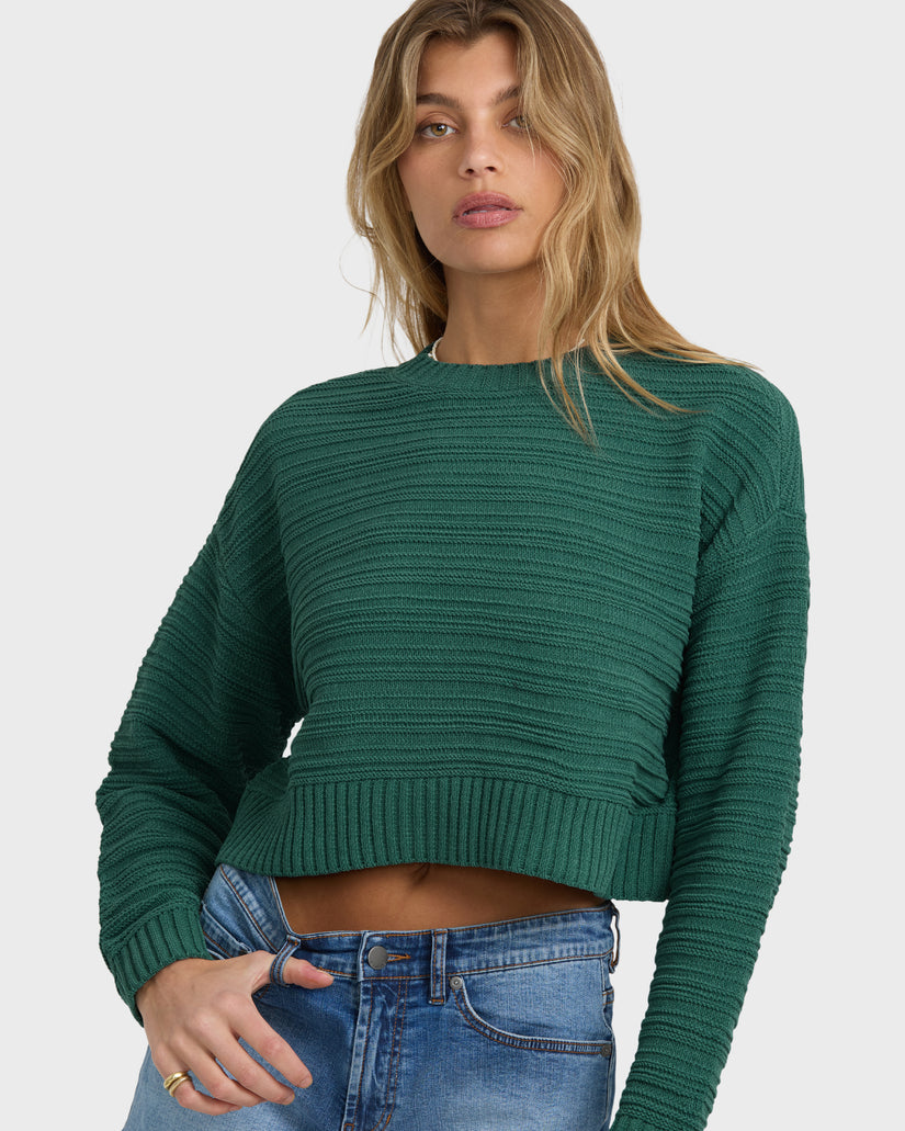 Green ribbed knit sweater with crew neckline and cropped length worn with blue jeans.